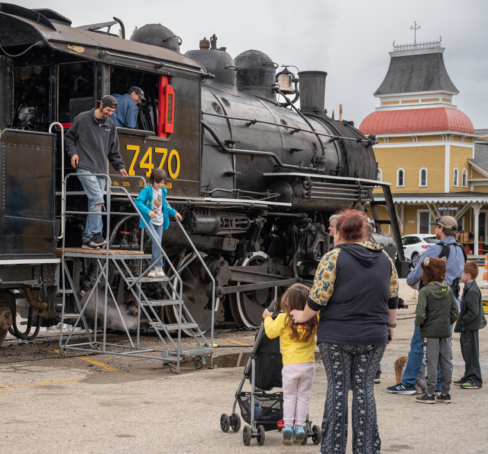 Man and boy take stairs down from locomotive cab as other people look on