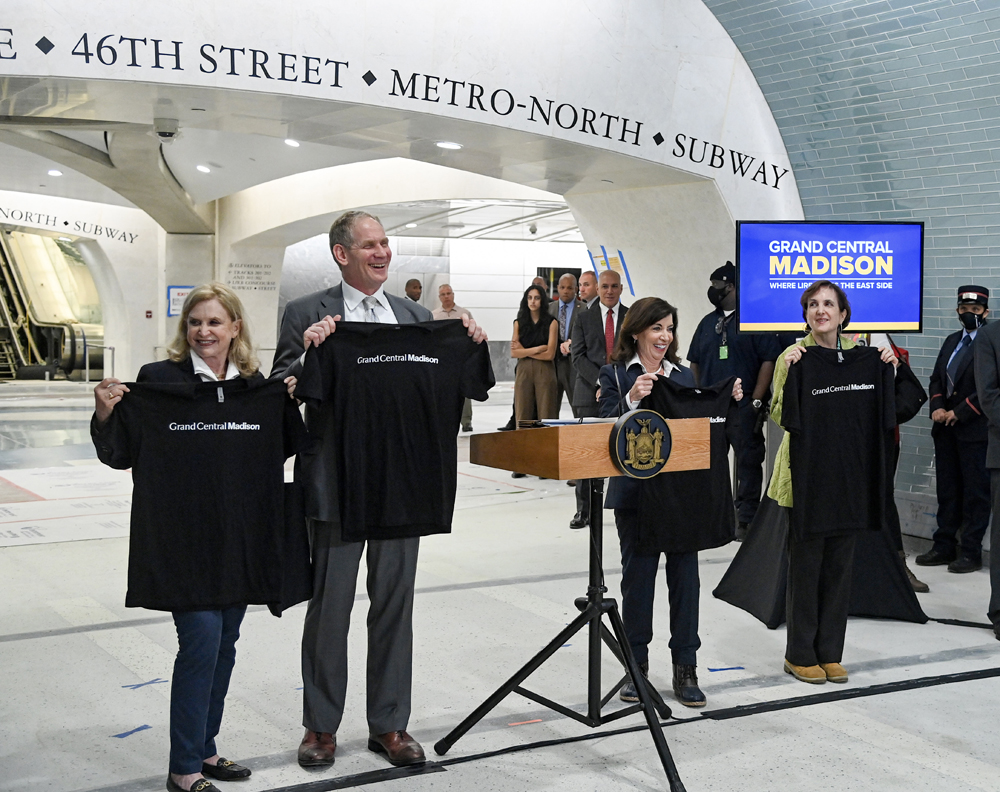 Four people in train station holding up T-shirts