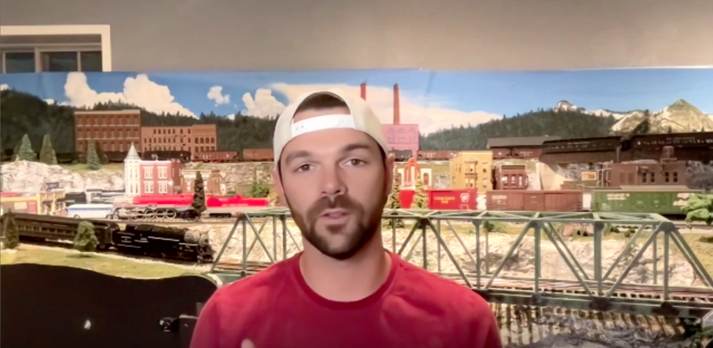 Bearded man with hat in front of toy train layout