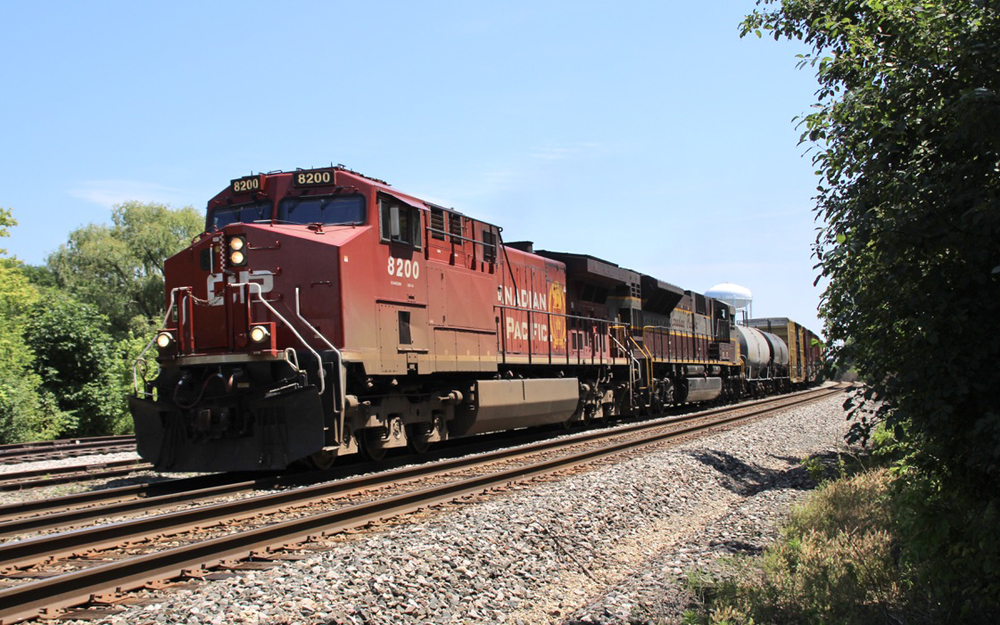 Red locomotive and one with maroon, gray, and yellow paint lead freight train