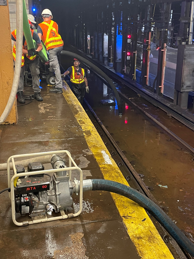 Men working along subway platform as pump removes water