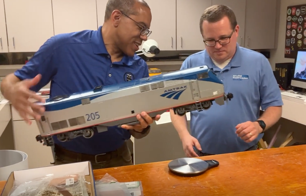 Two men holding a large scale Amtrak locomotive.