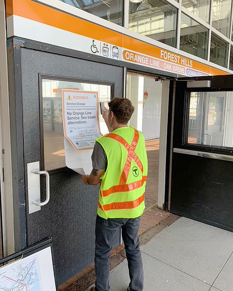 Man in high-visibility vest placing sign at rapid-transit station