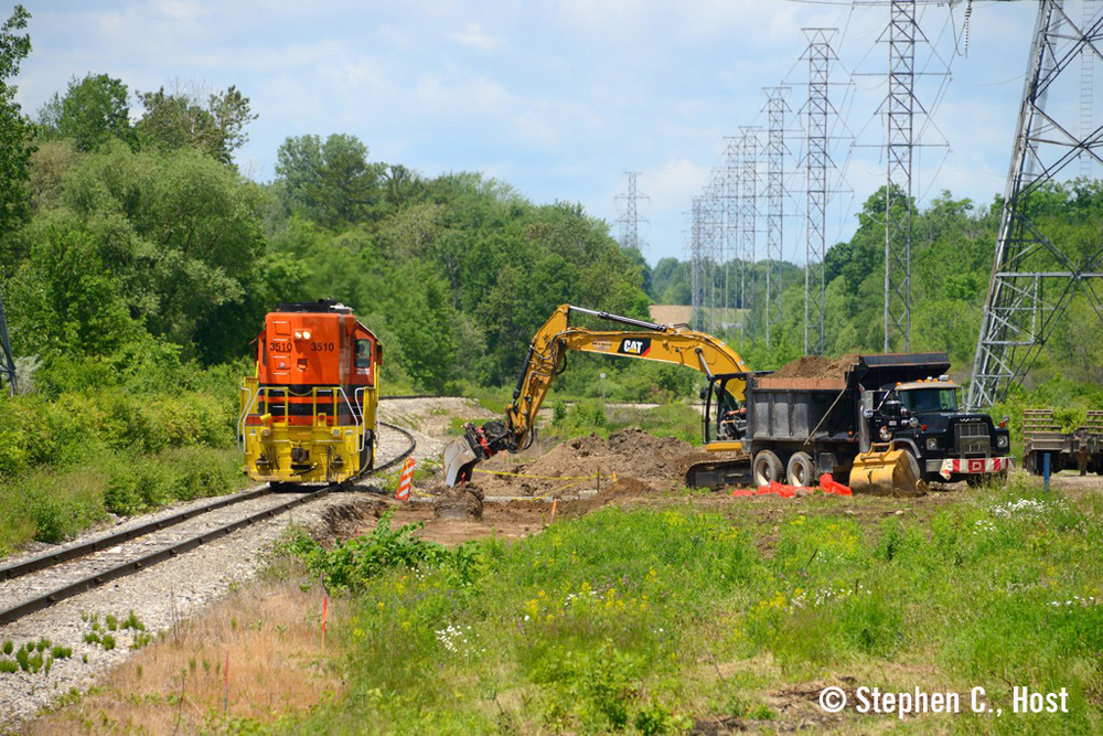 Orange locomotive passes construction equipment at work