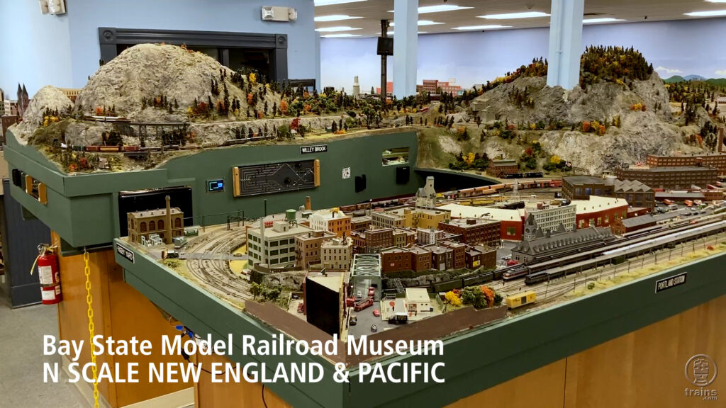 An overall view of a U-shaped N scale model railroad featuring a city in the foreground and mountains behind