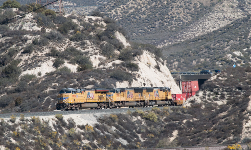 Three yellow painted locomotives lead a train through an arid landscape.