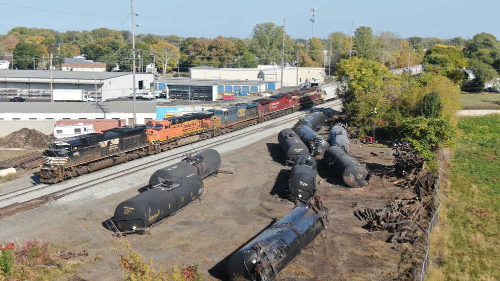 Train with five locomotives passes cars waiting to be removed after derailment