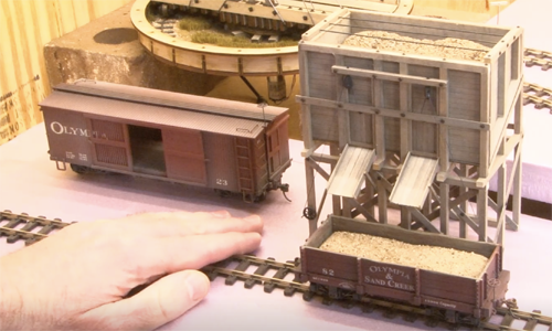 Hand gesturing to an unfinished model train layout.