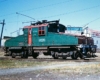 Green-and-red electric locomotive behind gas station