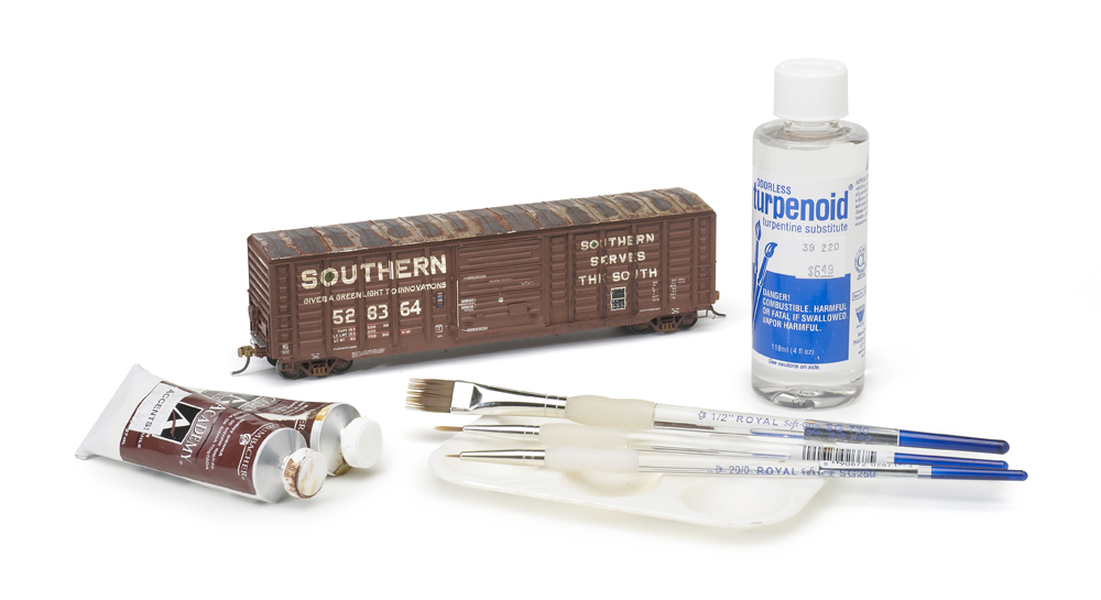 weathering with artist's oils: An image of a brown model boxcar alongside paints and brushes against white background.