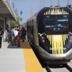 People mill about on platform next to streamlined passenger trains