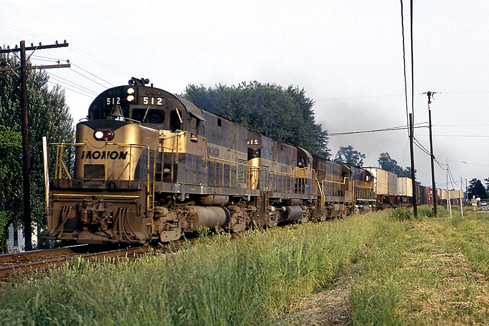 Four black-and-gold Monon Railroad diesel locomotives with freight train on curve