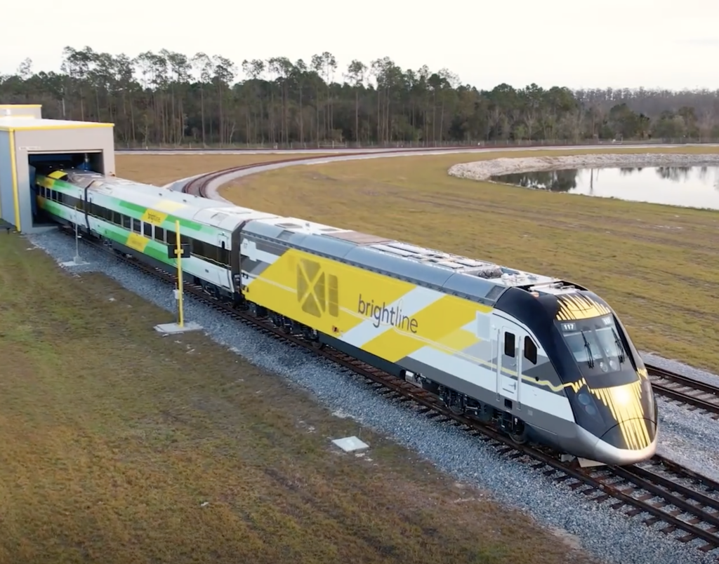 Yellow, white, and green striped train near a pond in a flat landscape.
