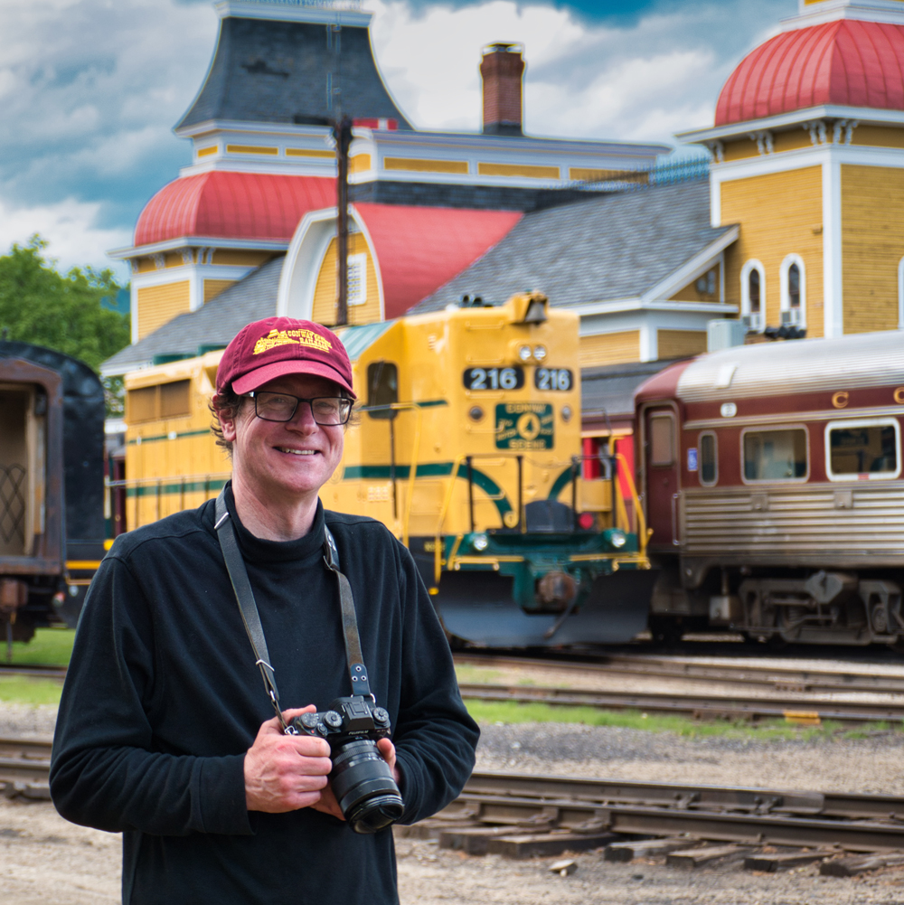 man holding camera with yellow train in background