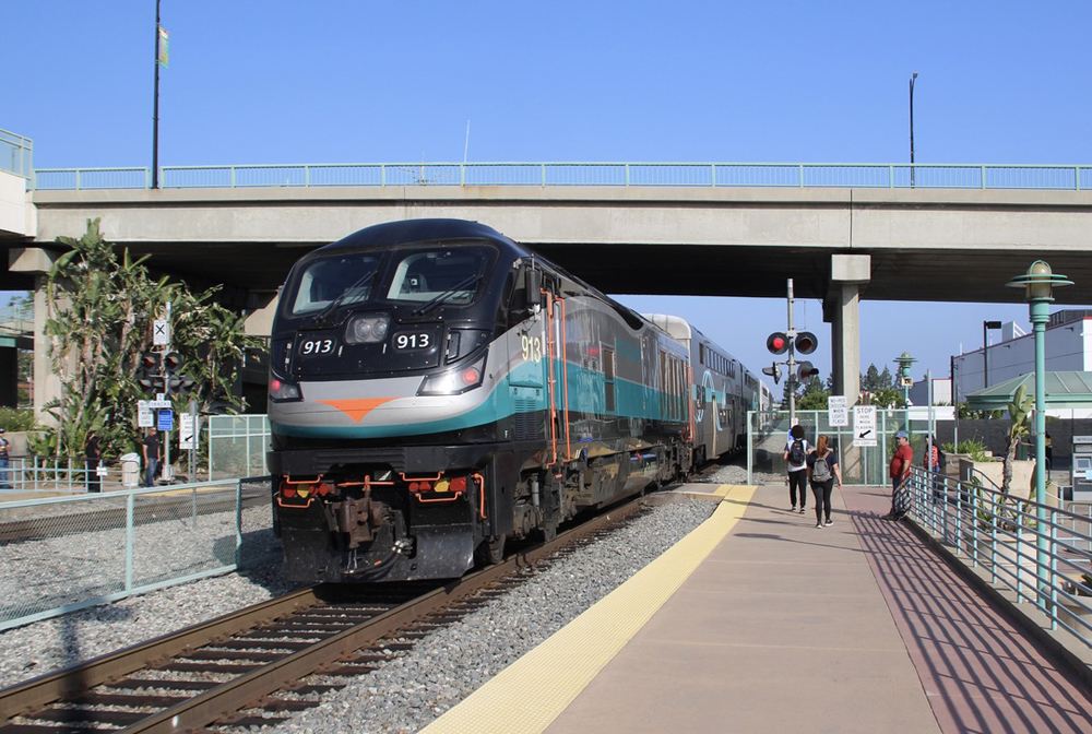 Silver, teal, and black locomotive pushes train out of station