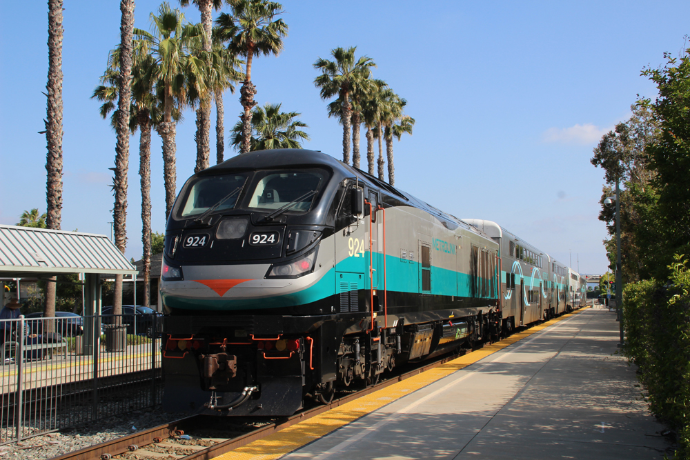 silver, black and teal train with palm trees in back