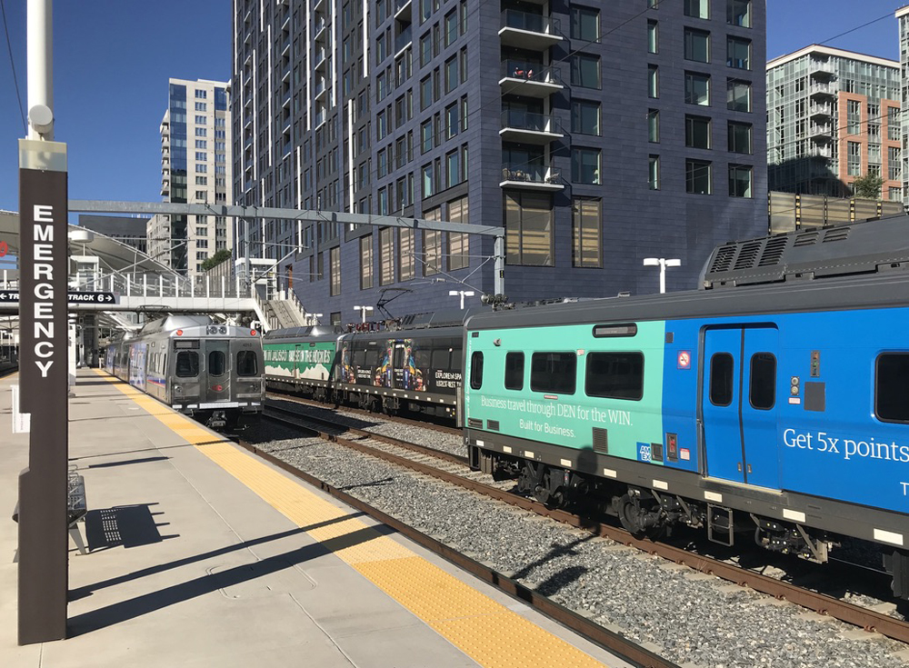 Commuter trains at station platform with multi-story buildings in background