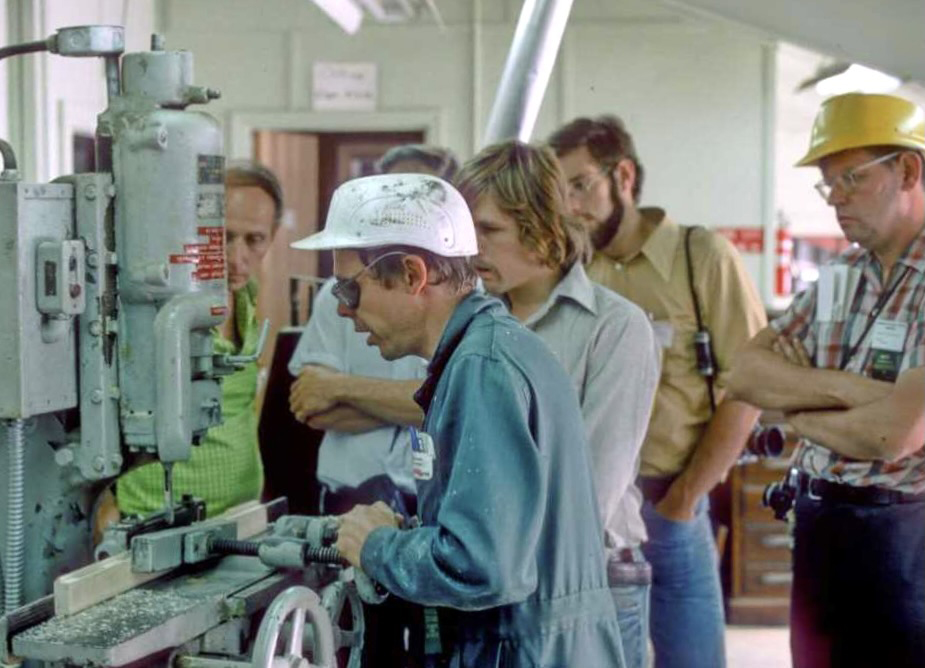 Man with hard hat works at large machine as others watch