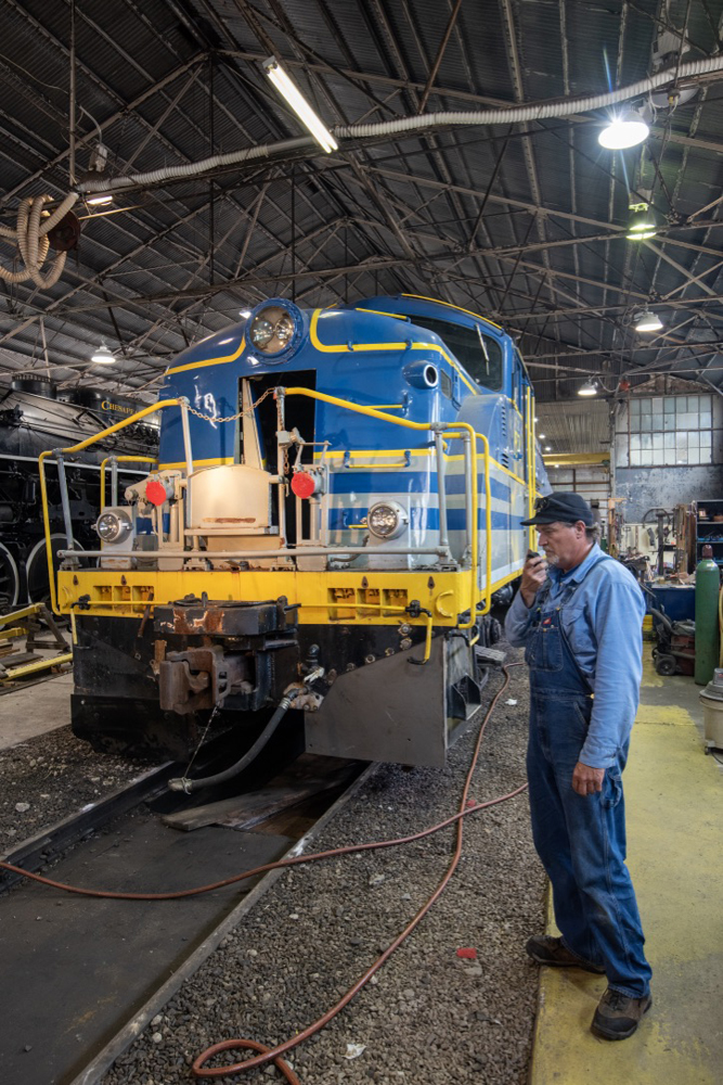 Man stands in front of blue and yellow diesel