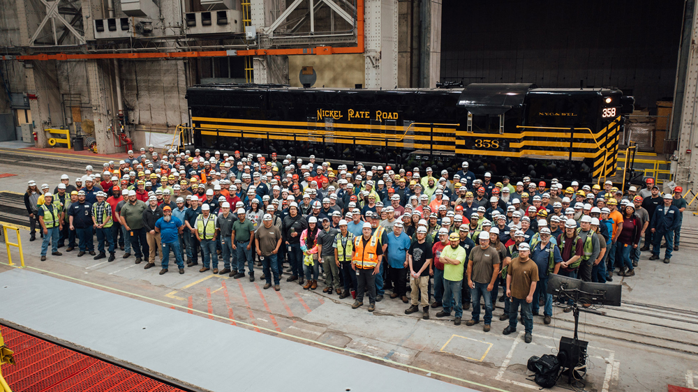 Large group of people pose with black and gold locomotive