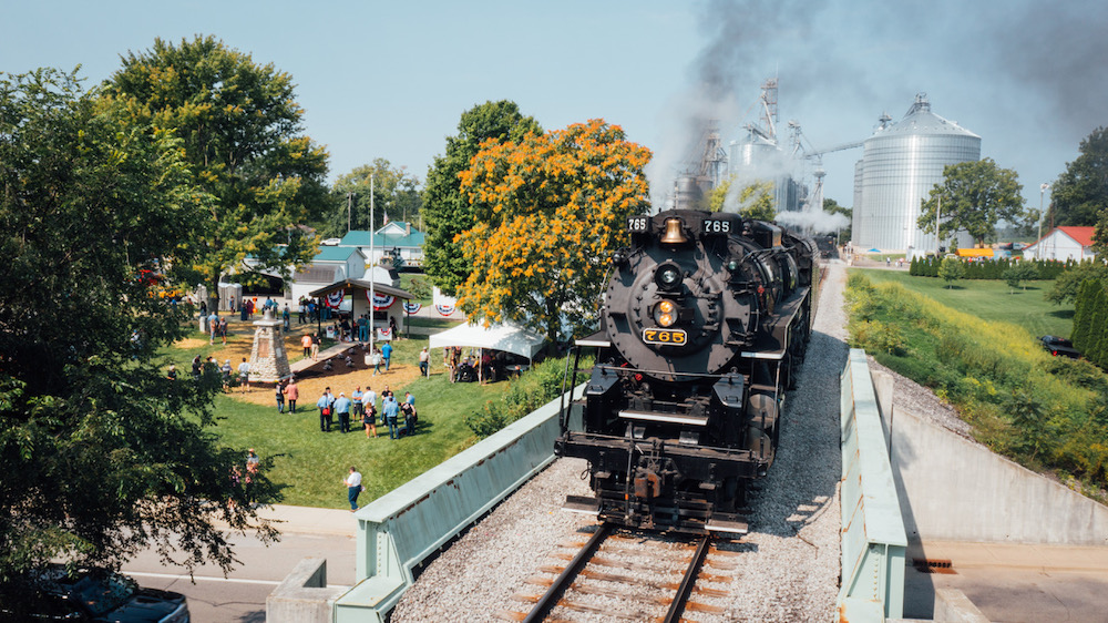 Steam locomotive sits on bridge during ceremony.