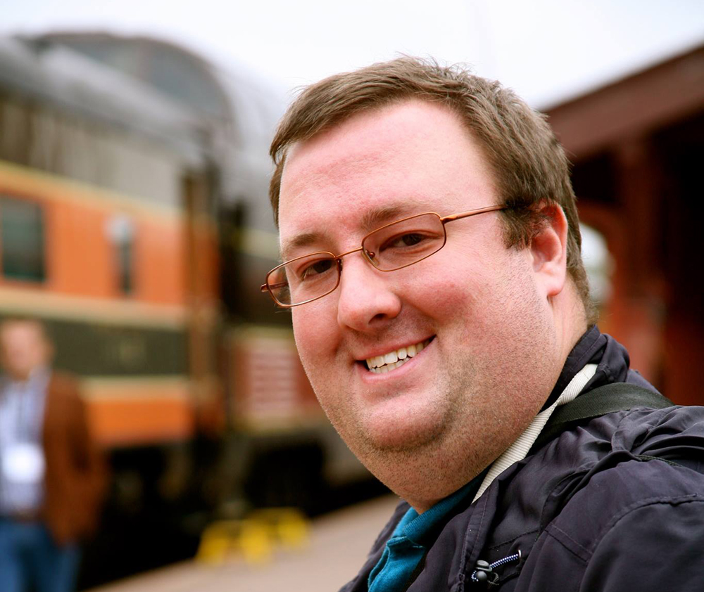 closeup of man with glasses and train in background