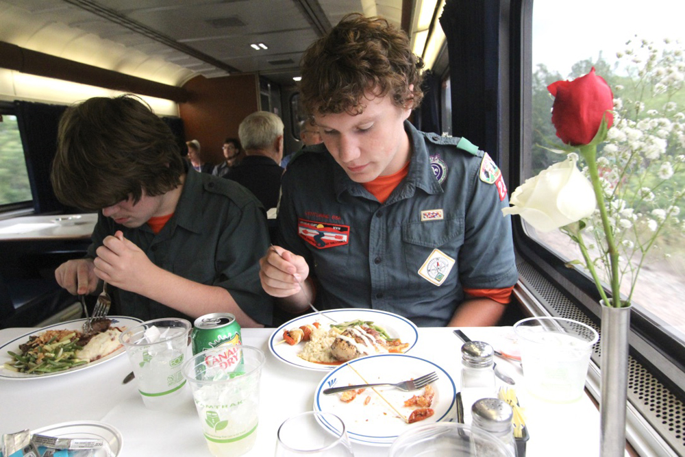 Two scouts in uniform eating at table with linen table cloth and flower in vase