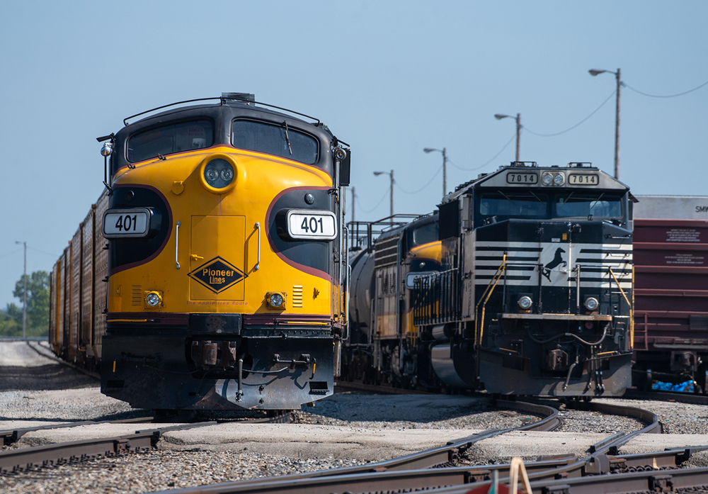 Black and yellow F-unit in yard, with another visible behind Norfolk Southern diesel