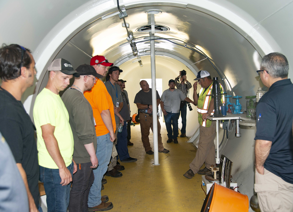 People listen to instructor while standing inside of tank car