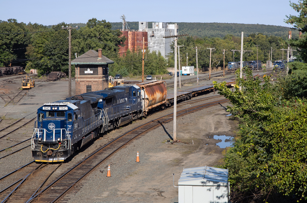 Train with two blue locomotives passes tower at yard
