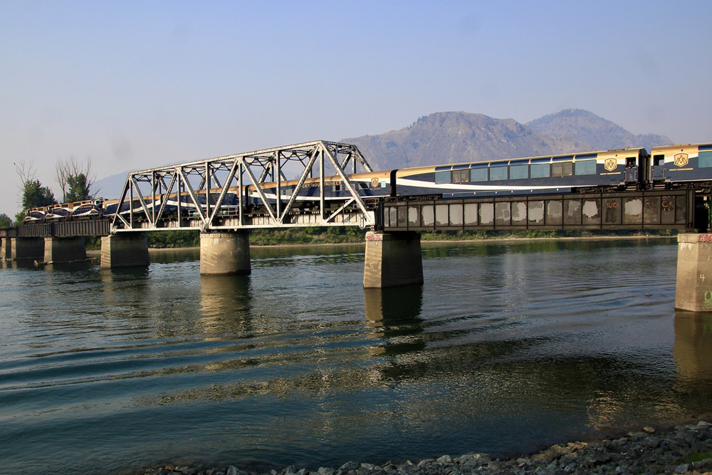 Passenger train crossing bridge across wide river