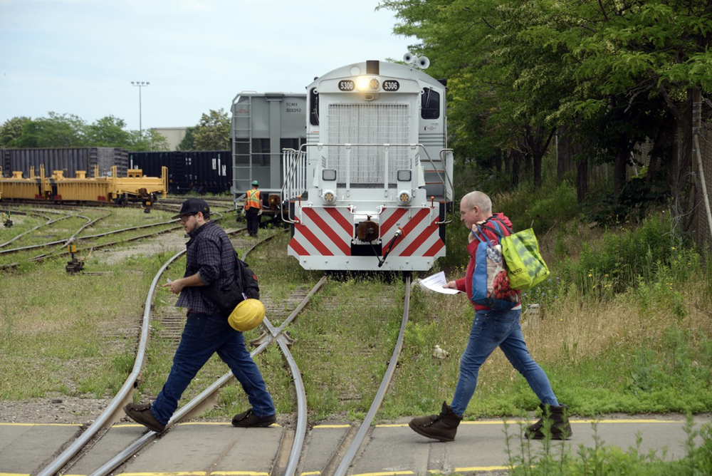 Two men walk across railroad tracks at manufacturing facility