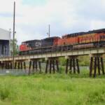 Train on bridge approaching small building covering tracks