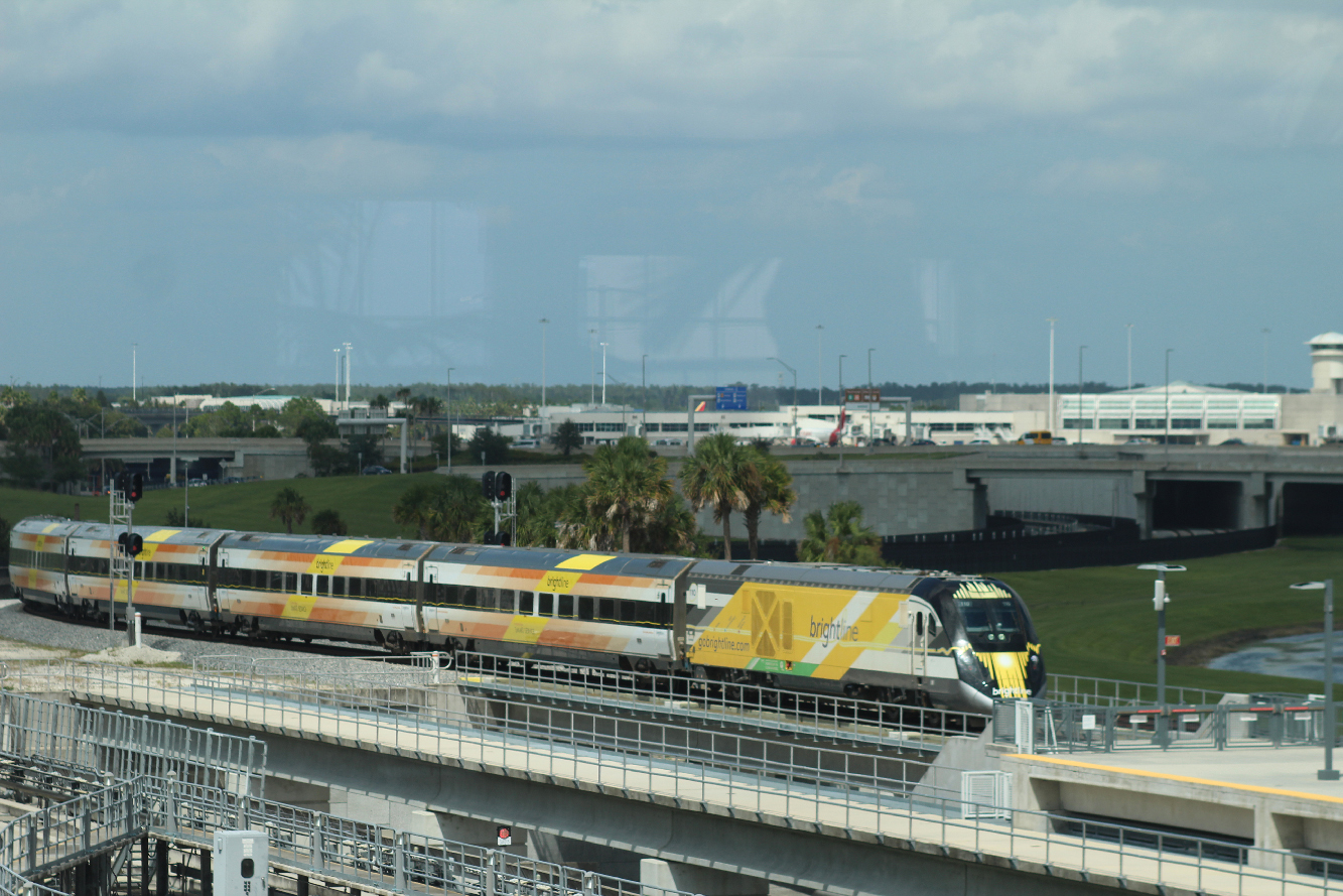Yellow, white, and black passenger train arriving at station. Brightline inaugurates Orlando service.