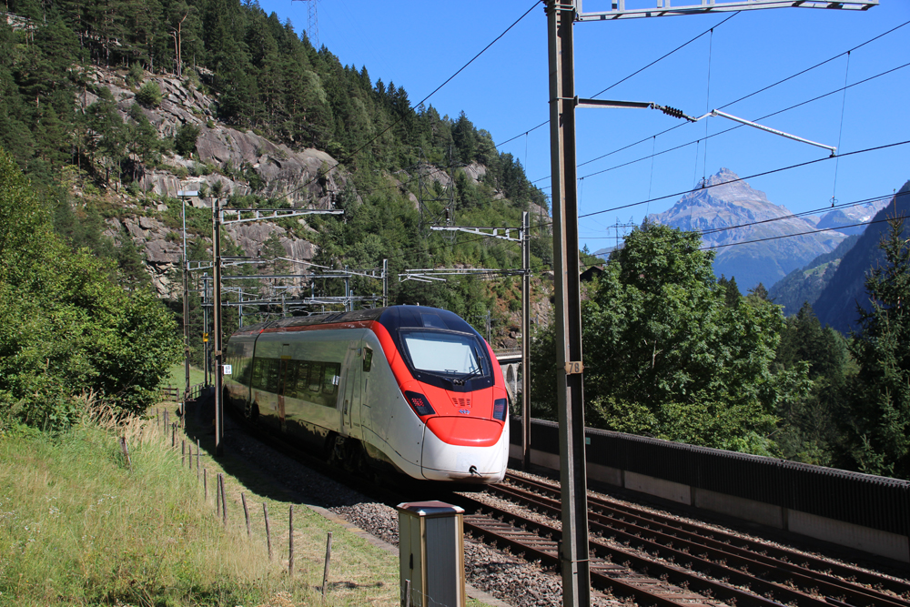 Red and while electric passenger train on curve with Alps in the background