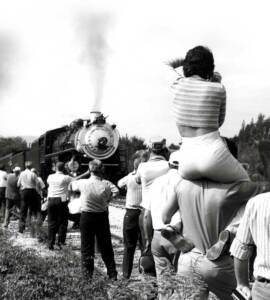 Woman sits on man's shoulders to view steam locomotive