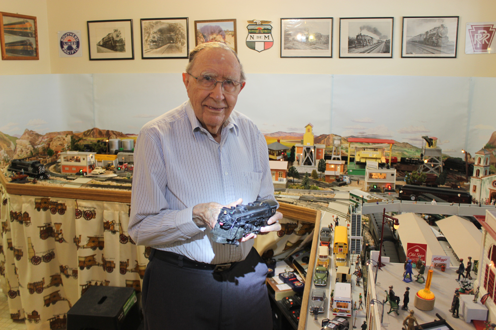 man holding model locomotive next to layout