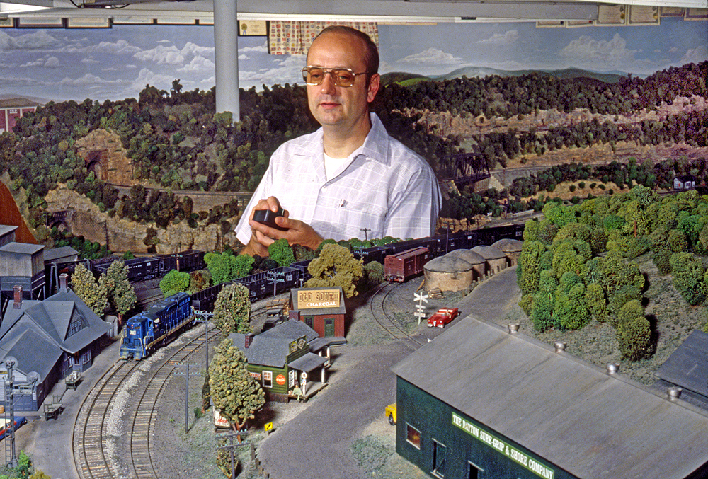 A man in a white shirt stands in the midst of an Appalachian scene on a model railroad