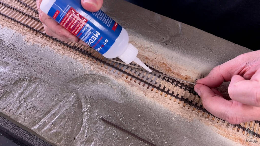 A person is applying glue to pieces of model railroad track