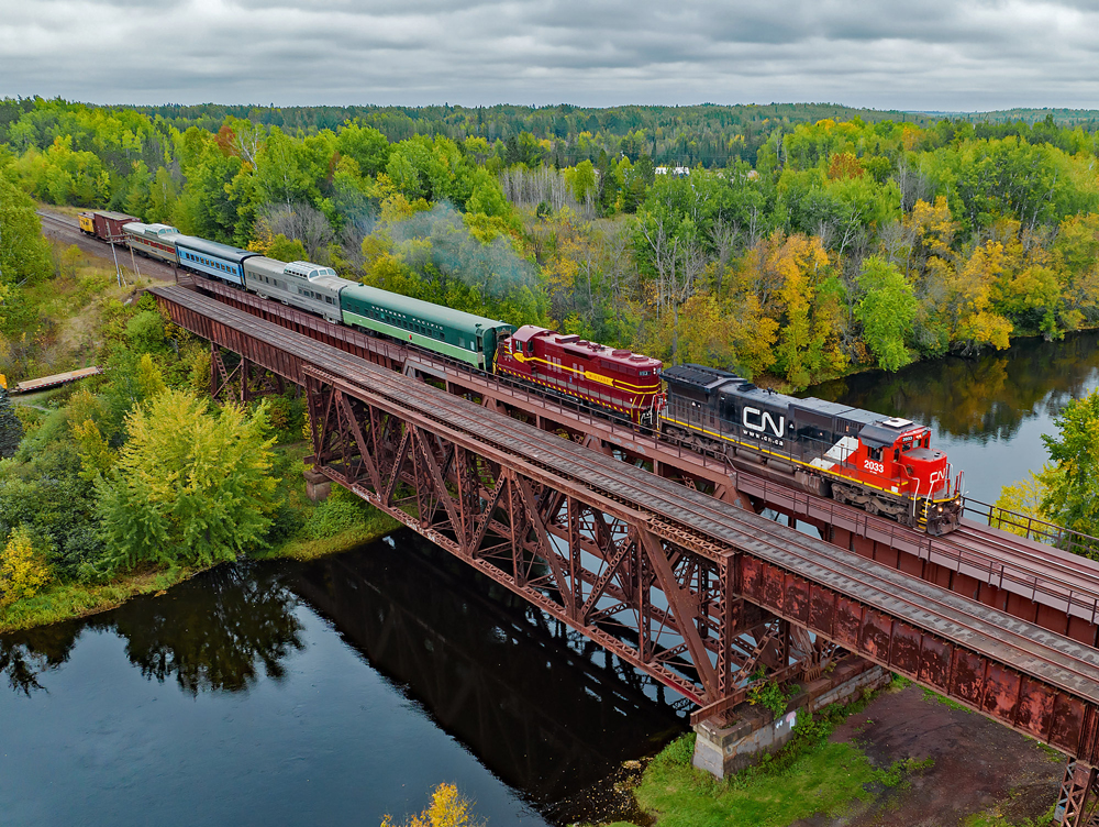 Passenger train with two diesel locomotives crossing a bridge over a river.