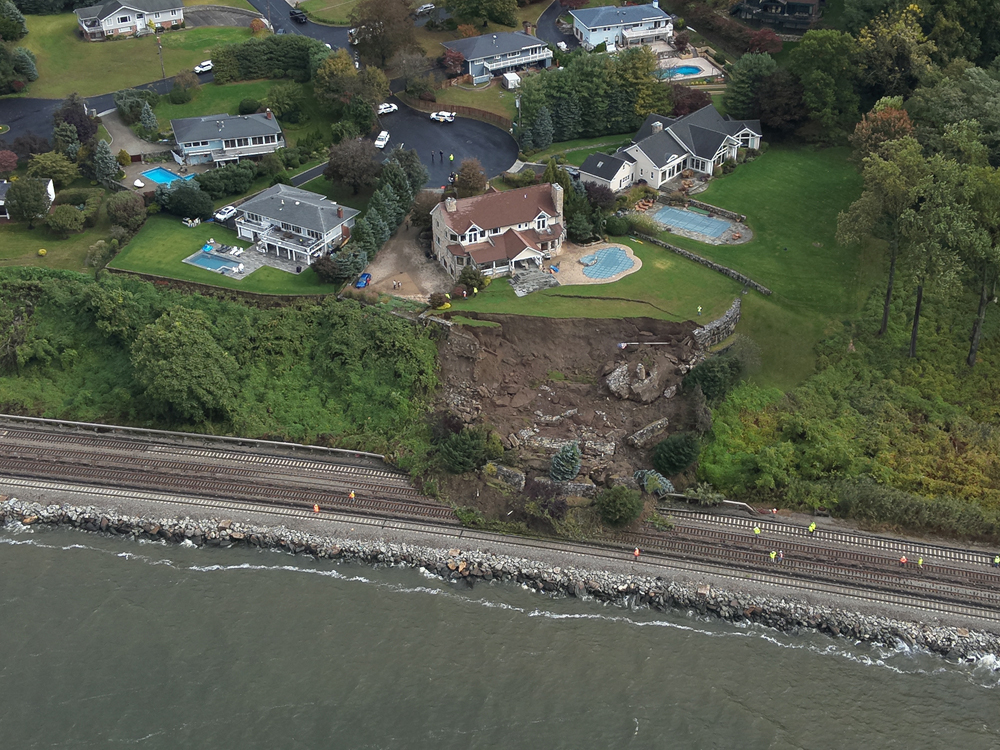 Aerial view of mudslide from just behind large house onto railroad tracks.