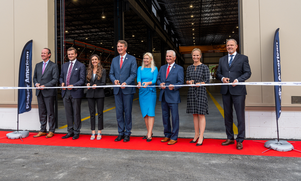 Eight people posed for ribbon-cutting ceremony in front of factory door.