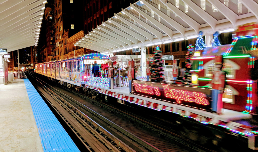 Decorated rapid-transit train with trailing flatcar featuring Santa Claus