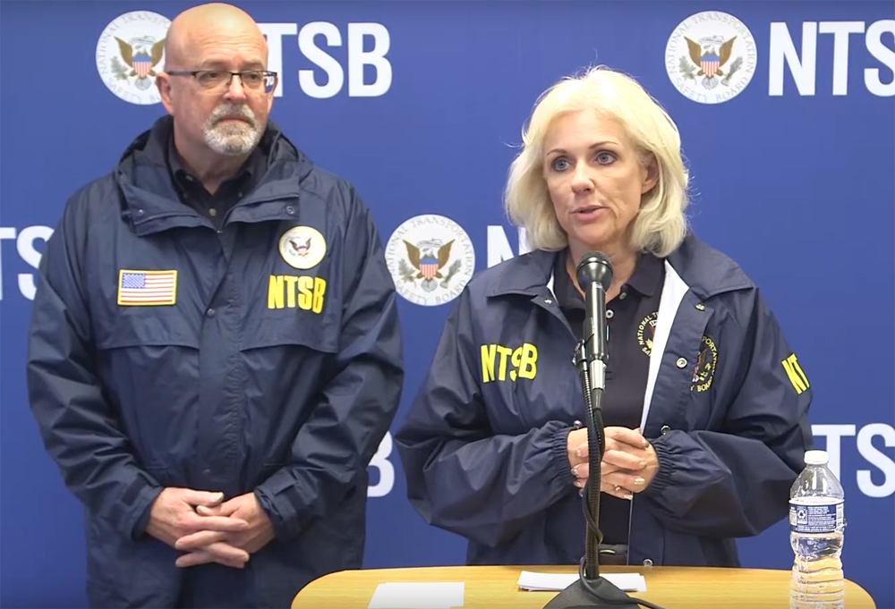 Man and woman in jackets labeled "NTSB" address media briefing