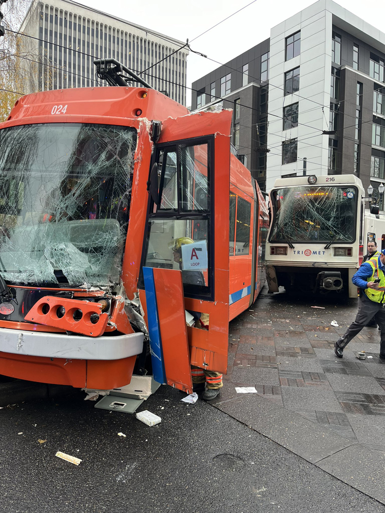 Orange streetcar and white light rail train in intersection after collision