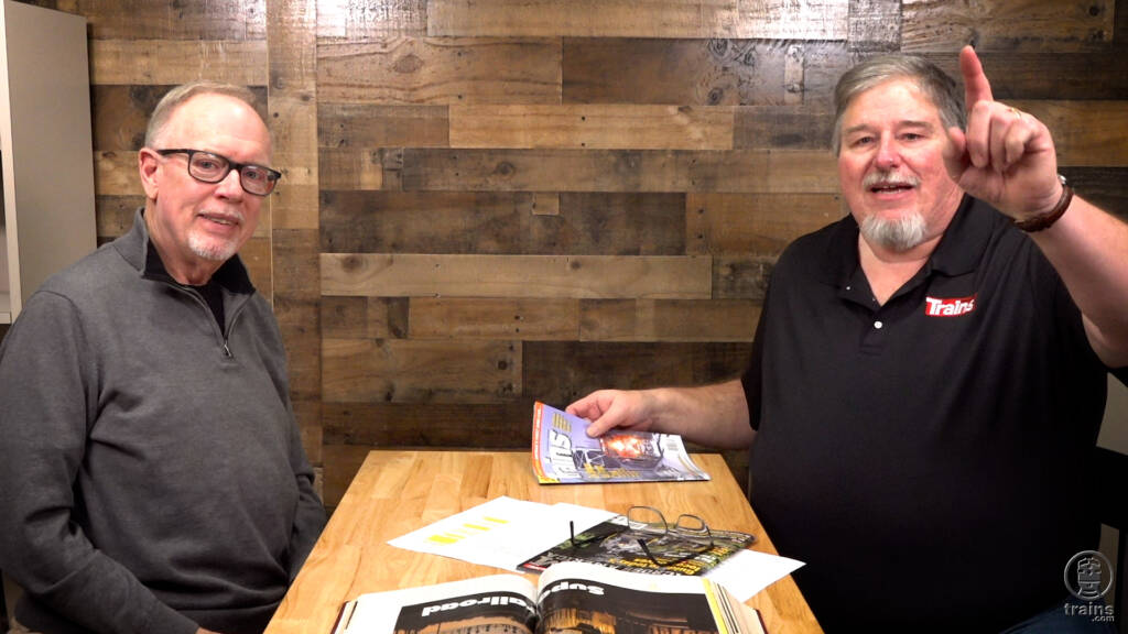 Two men seated at a table for an interview. Trains milestone.