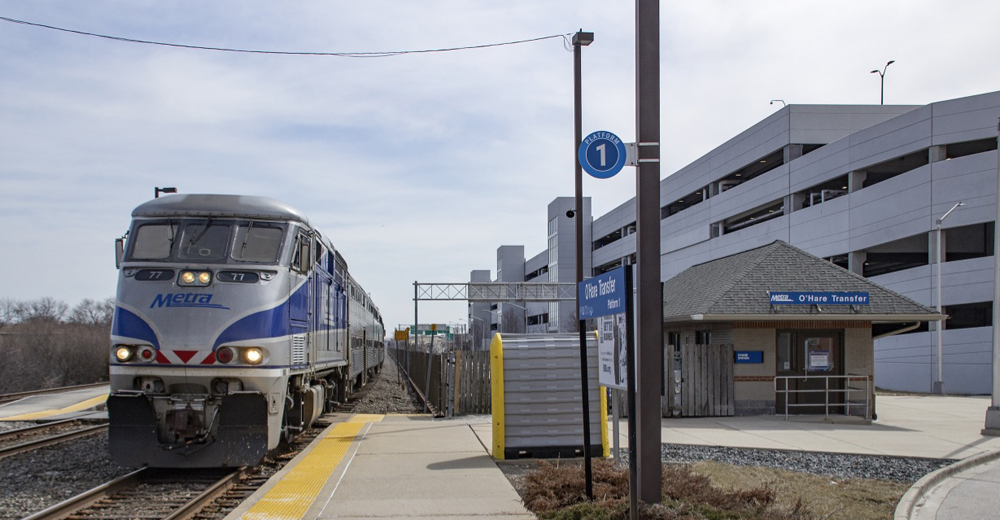 Commuter train stopping at station with large parking structure in background