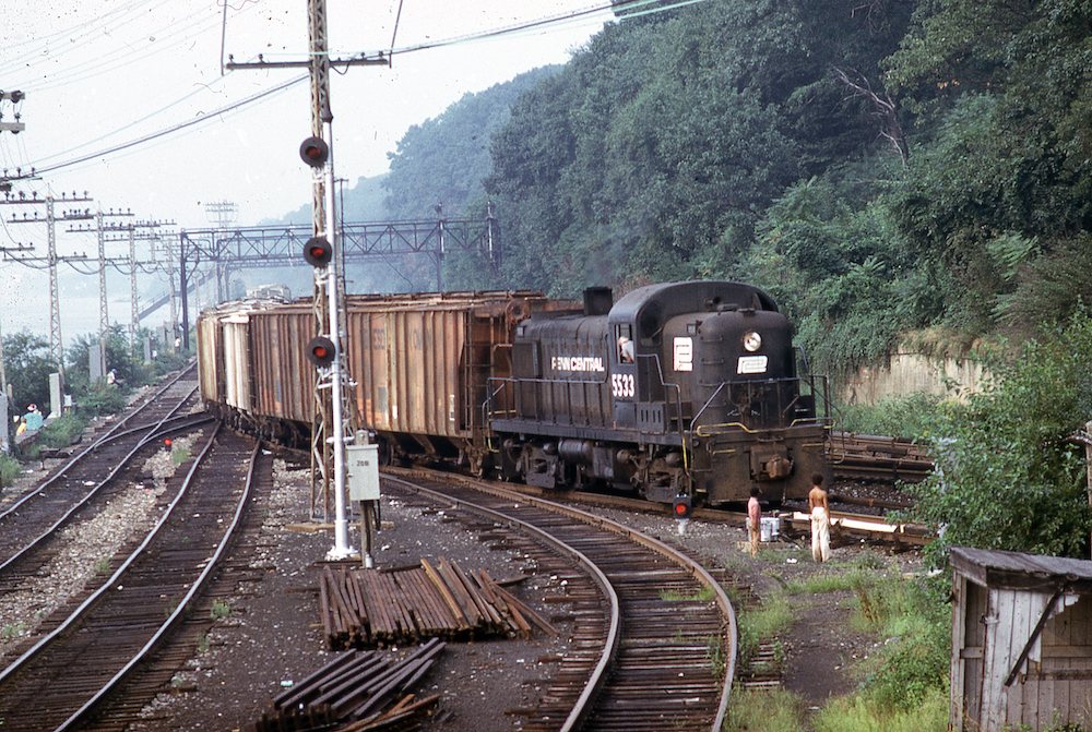 A black engine with train in tow curves off a mainline into a siding