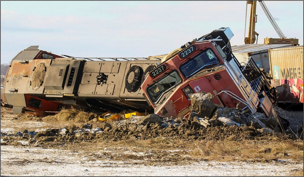 Two derailed locomotives partially buried in dirt with containers visible in the background