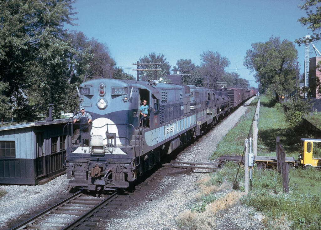 Blue-and-gray Train Master diesel locomotive with freight train at crossing